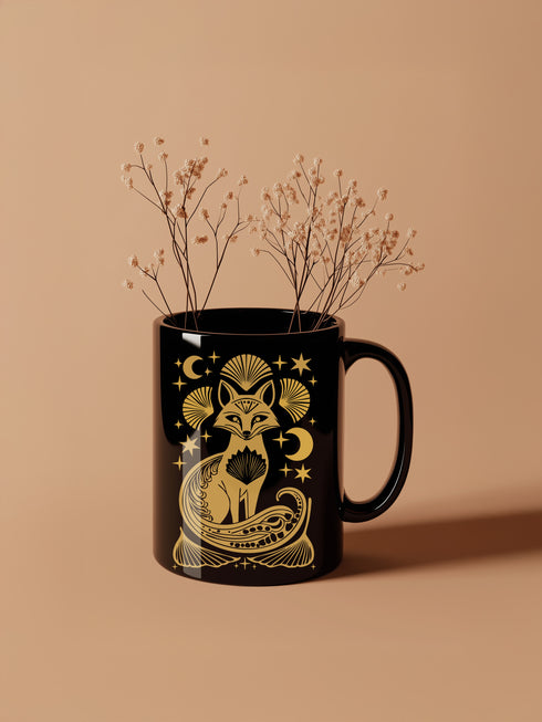 A black ceramic mug featuring a stylized golden fox design surrounded by Art Deco ginkgo fans, crescent moons, and stars. The mug has a glossy finish and ergonomic handle.